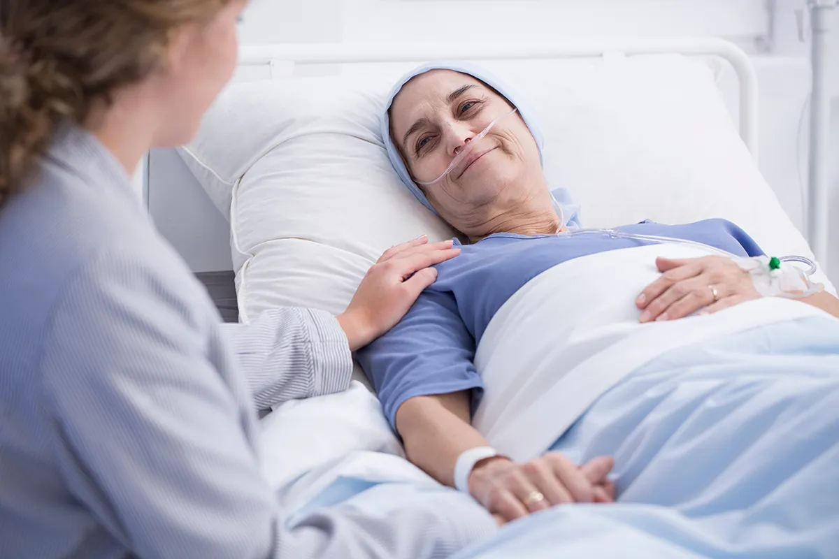 Femme allongée sur un lit d'hôpital souris à une proche qui lui fait face