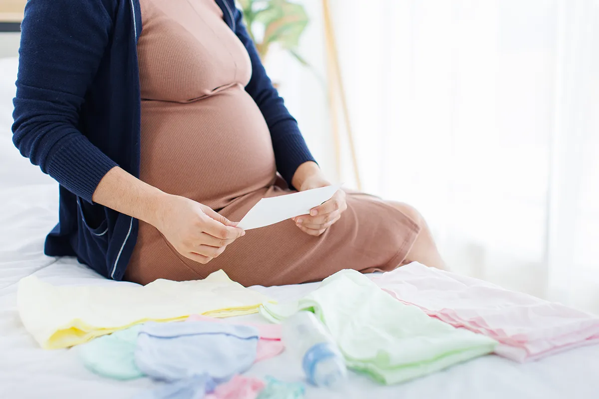 Femme enceinte préparant l’arrivée du bébé avec des vêtements et accessoires de maternité.