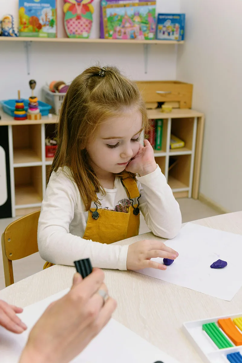 Enfant en séance de motricité fine avec pâte à modeler dans une salle de prise en charge pédiatrique.