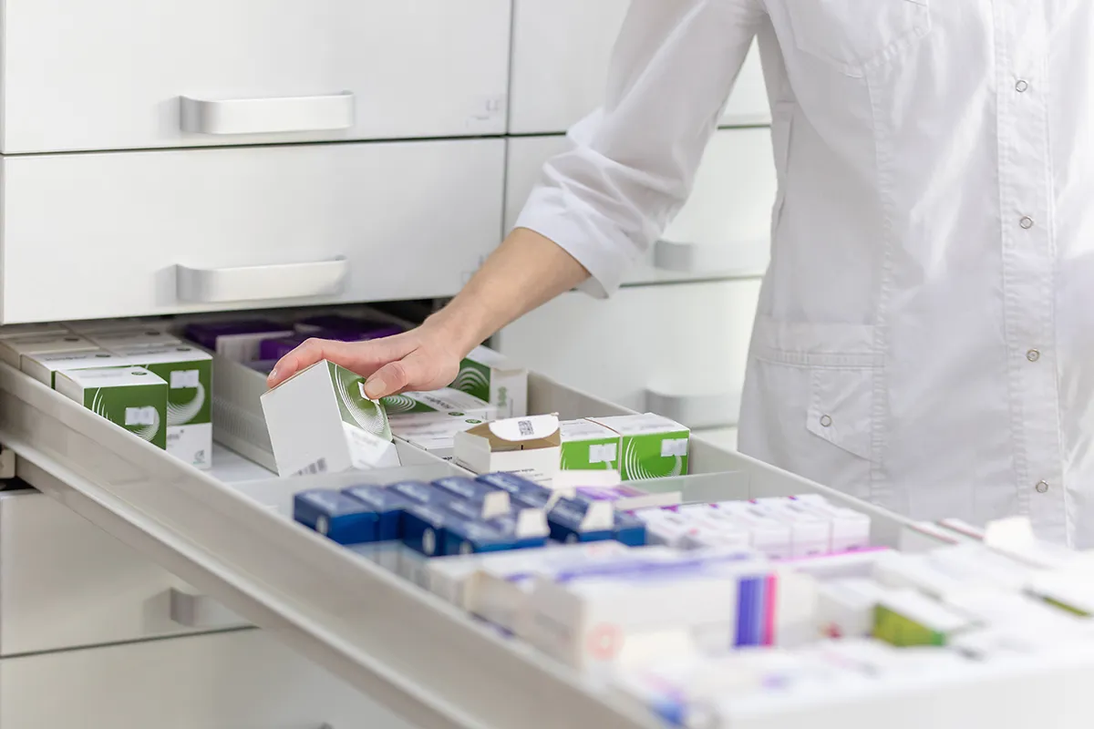 Pharmacienne rangeant des boîtes de médicaments dans un tiroir de pharmacie.