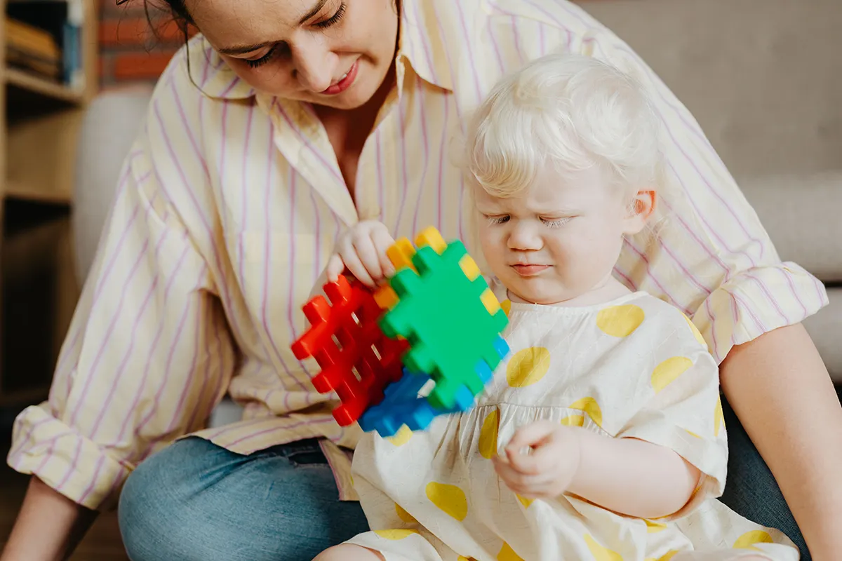 Jeune enfant jouant avec un cube coloré aux côtés d’une adulte.