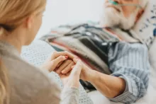 Patient âgé sur un lit d'hôpital tient la main d'un proche