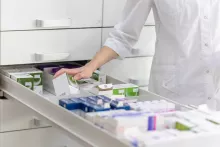 Pharmacienne rangeant des boîtes de médicaments dans un tiroir de pharmacie.