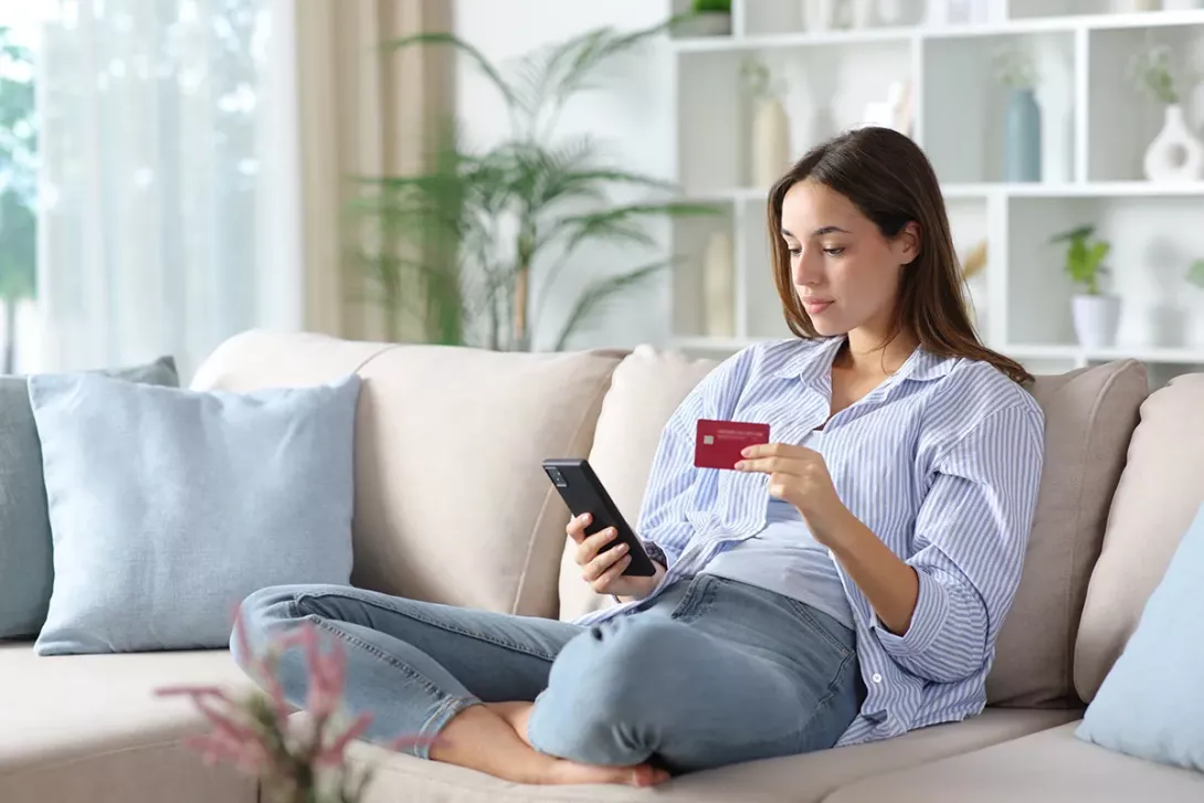 Femme sur un canapé, fait un don en ligne avec son téléphone pour le centre hospitalier de Carcassonne